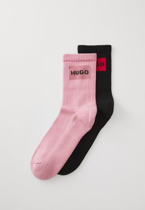 Pair of ribbed socks, one pink and one black, each with a rectangular logo patch featuring the word "HUGO" near the top cuff.