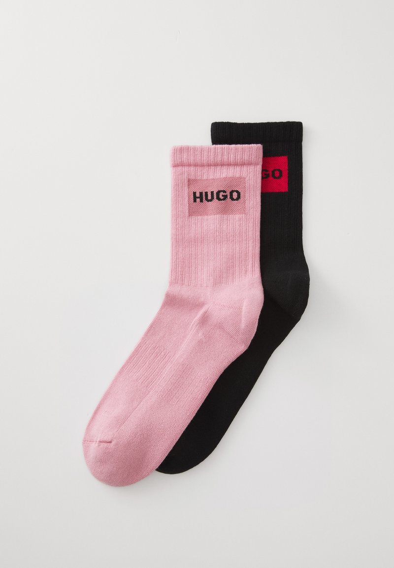Pair of ribbed socks, one pink and one black, each with a rectangular logo patch featuring the word "HUGO" near the top cuff.