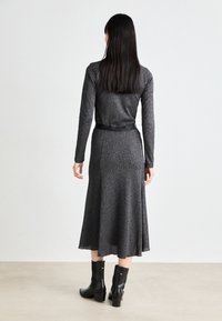 Gray, long-sleeve dress with a fitted bodice and flared skirt. Features a black belt at the waist and is made of textured, reflective fabric.