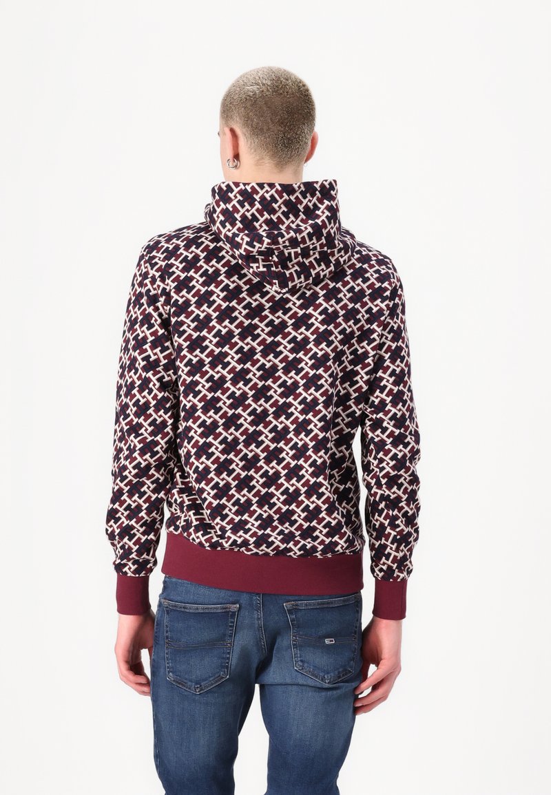 Felpa con cappuccio caratterizzata da un motivo geometrico bordeaux e bianco, con polsini e orlo a costine. Indossata con jeans blu.