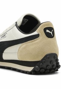 Puma sneakers met een witte leren bovenkant, zwarte suède accenten, een tan suède hiel en een rubberen zool met ronde studs voor grip.