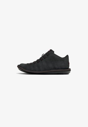 Sneaker in suede nero con profilo basso, upper texturizzato, lacci elastici e suola in gomma caratterizzata da un sottile accento rosso e punta arrotondata.