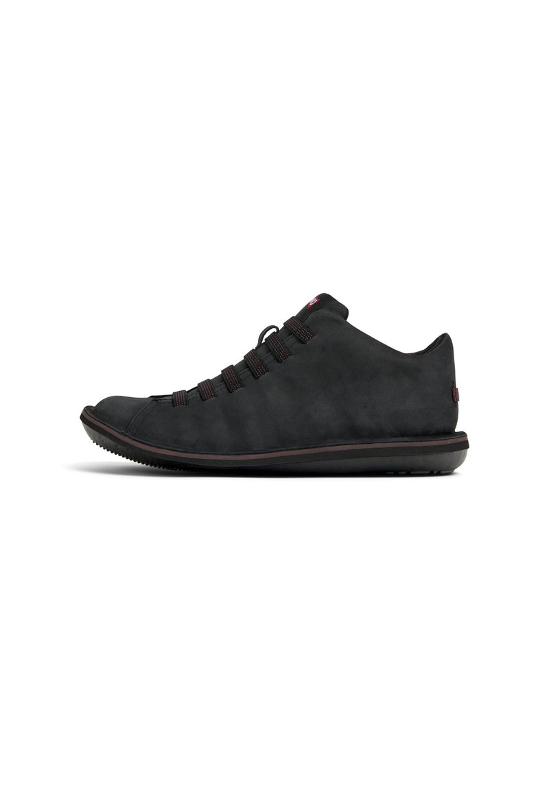 Sneaker in suede nero con profilo basso, upper texturizzato, lacci elastici e suola in gomma caratterizzata da un sottile accento rosso e punta arrotondata.