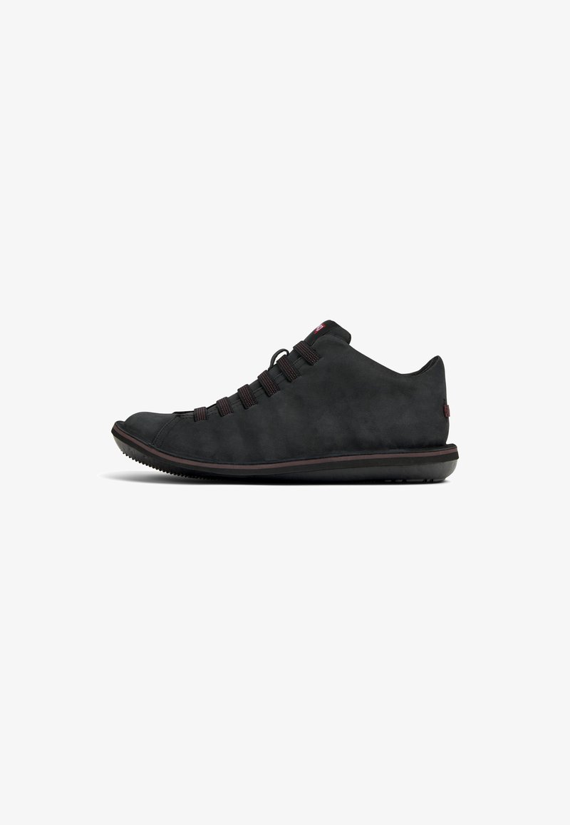Black suede sneaker with a low profile, textured upper, elastic laces, and a rubber sole featuring a subtle red accent and rounded toe.