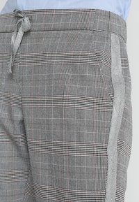 Spodnie w kratę w odcieniach szarości i czerni, z elastycznym pasem na sznurek, subtelną teksturą oraz bocznymi paskami w kontrastującym jasnoszarym kolorze.