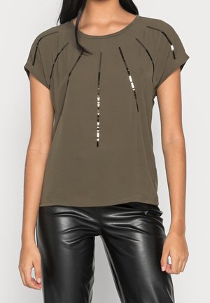 Woman wearing olive green short-sleeve top with vertical black and silver sequin lines, paired with black leather pants.