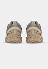 Sapatos de exterior castanhos e bege com solas salpicadas, tecido texturizado, colarinhos acolchoados e detalhes verdes no calcanhar e na língua.