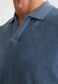 Blauwe gebreide polo met een gestructureerde afwerking, voorzien van een klassieke kraag en een diep V-halsontwerp. Zachte, lichtgewicht stof.