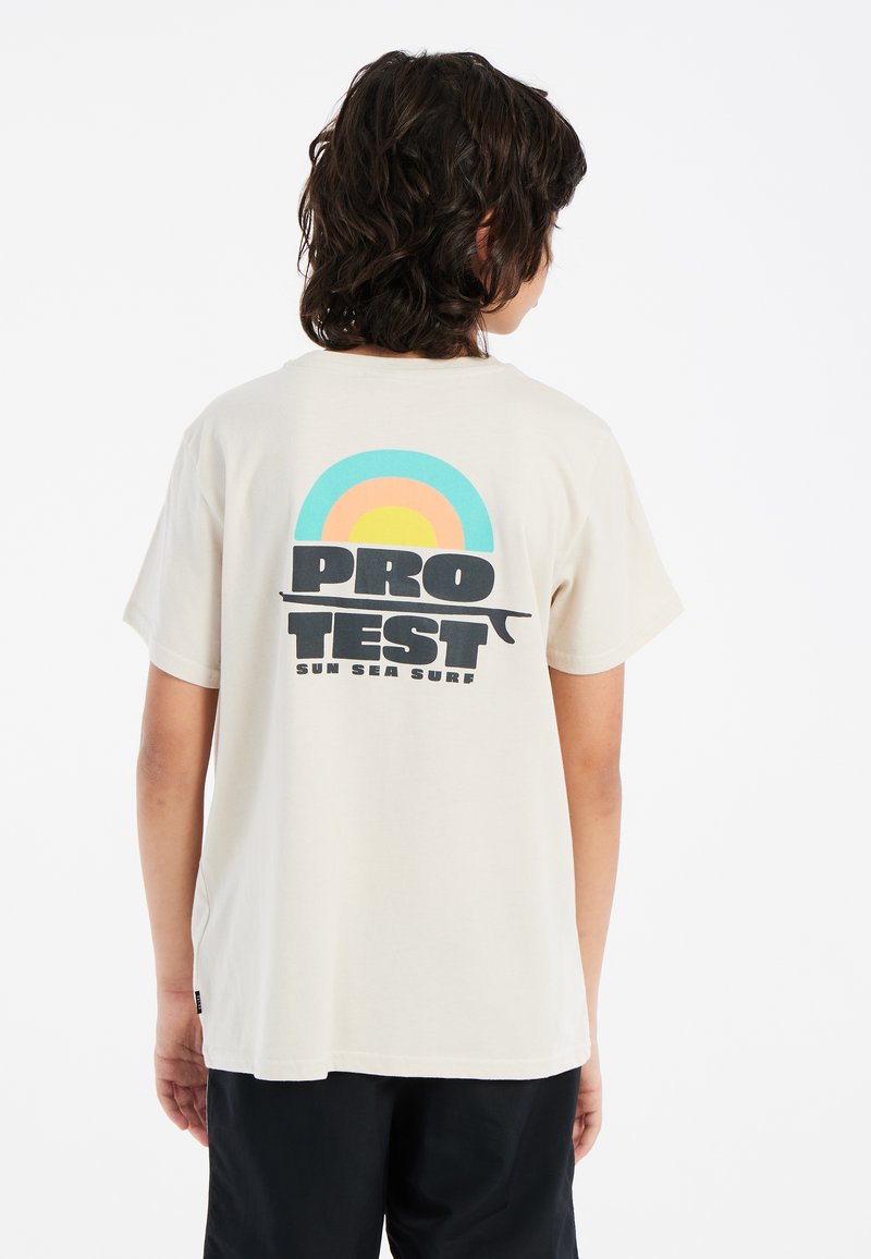 Šviesiai rudos spalvos medvilnės marškinėliai su grafiniu dizainu, kuriame mėlyni, oranžiniai ir geltoni pusmėnuliai virš žodžio "PRO TEST" parašyto drąsiais juodais rašmenimis.