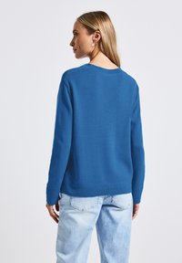Pull en tricot bleu avec un col rond et des poignets côtelés. Porté avec un denim délavé, il arbore une coupe décontractée et un tissu texturé.