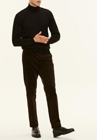Maglione nero a collo alto abbinato a pantaloni in velluto a coste marrone scuro e mocassini neri. Il maglione ha un design aderente; i pantaloni presentano un tessuto texturizzato.