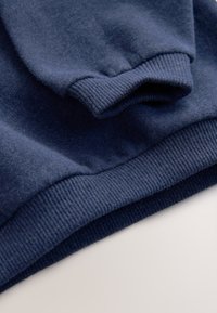 Tengerészkék pulóver, sima, puha textúrával, bordázott mandzsettákkal és szegéllyel, laza kialakítással, minták nélkül.