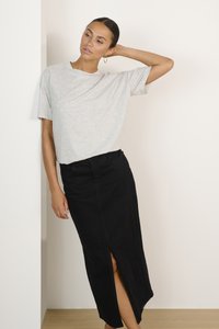 T-shirt gris clair à manches courtes avec une légère texture et une coupe décontractée, associé à une longue jupe en denim noire comportant une fente sur le côté.