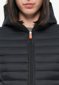 Zwarte gewatteerde jas met een rits, voorzien van een oranje ritslip. Het materiaal is glad, en het ontwerp heeft een capuchon en horizontale stiksels.