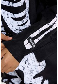 Black fabric jacket featuring a white skeleton design, textured print, and a label on the sleeve reading "SWEETME."
