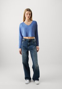 Svetlomodrý cropovaný sveter s výstrihom do V a rebrovanou textúrou v kombinácii s roztrhanými tmavomodrými širokými rifľami a bielymi teniskami.