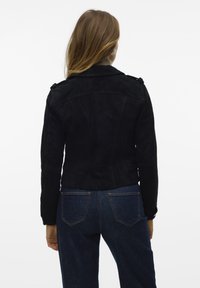 Svart mockajacka med en åtsittande design, med axelremmar och en slät yta, tillsammans med mörkblå jeans.