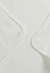 Pehmeä valkoinen tekstiili, jossa on plush-tekstuuria, kahden päällekkäisen kulman ja sujuvien reunojen kanssa, luoden saumattoman ja kotoisan ilmeen.