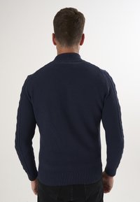 Marineblauer, gestrickter Pullover mit strukturiertem Muster, geripptem Kragen und Bündchen, mit Kabeldetails entlang der Ärmel. Rückansicht gezeigt.