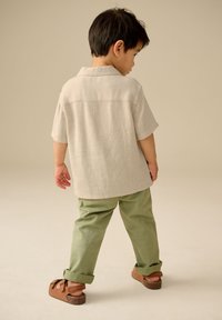 Lichtbeige overhemd met korte mouwen en een gestructureerde afwerking, gecombineerd met opgerolde olijfgroene broek en bruine sandalen.