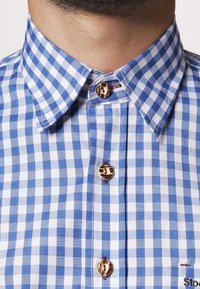 Camisa a cuadros azul y blanca con cuello abotonado, que presenta botones de carey y sutiles acentos rojos cerca de la tapeta.