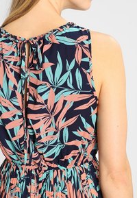 Abito senza maniche con sfondo blu navy che presenta una stampa botanica in rosa e teal. Vita arricciata e dettaglio con fiocco sul retro del collo.