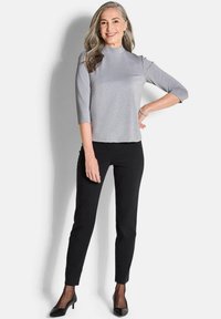 Graues, tailliertes Oberteil mit dreiviertel Ärmel und Stehkragen, kombiniert mit schwarzen schmal geschnittenen Hosen und schwarzen High Heels. Glatte Textur mit einem dezenten Glanz.