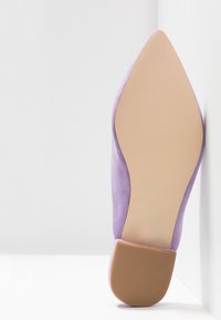 Chaussure en daim violet à bout pointu avec un design lisse et effilé, et une semelle beige texturée. Le talon est bas et plat.