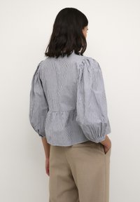 Gestreepte blouse met pofmouwen, getailleerd lijfje en peplum taille. Blauw en witte strepen, lichte stof, casual ontwerp. Gecombineerd met beige broeken.