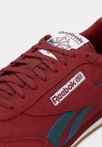 Červené semišové tenisky Reebok so bielym jazykom s logom, tmavými tealovými a modrými akcentmi, plochými šnúrkami a gumovou podrážkou.
