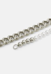 Bracelet en chaîne métallique et perles, présentant des maillons argentés brillants, des boules métalliques alternées et des perles blanches, avec un détail de fermoir rond.