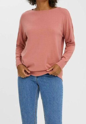 Pull en tricot rose clair à manches longues avec un décolleté bateau et une coupe légèrement oversize, associé à un jean en denim bleu.
