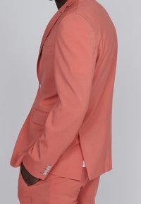 Giacca da abito corallo realizzata in tessuto leggero, con rever a notchetto, tasca laterale e quattro bottoni decorativi sui polsini. Vestibilità su misura.