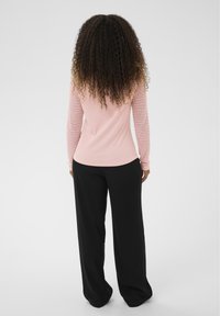 Top met lange mouwen in lichtroze met gestructureerde, patroonmouwen; gecombineerd met losvallende zwarte broek. Licht gebogen zoomlijn.