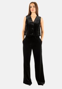 Veste en velours noir courte avec un décolleté en V et des boutons, associée à un pantalon large en velours noir. Les deux pièces présentent une texture lisse.