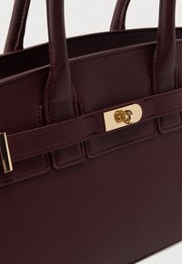 Sac à main en cuir bordeaux avec deux poignées, une texture lisse, une fermeture à fermoir doré et des accents de design rectangulaires pour plus de détails.