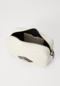 Borsa rettangolare bianca realizzata in materiale sintetico. Presenta una chiusura con zip, fodera interna nera e un logo a forma di diamante su un lato.