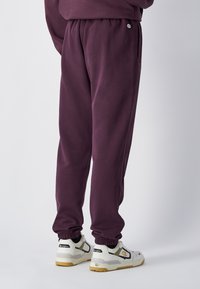 Paarse trainingsbroek met elastische boorden, zijzakken en een koordsluiting in de taille. Gecombineerd met wit en grijze sneakers met accenten.