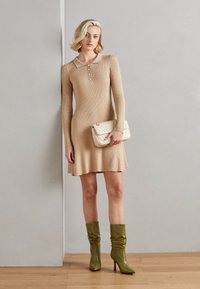 Beige neulemekko pitkillä hihoilla ja kauluksella, jossa nappilista. Yhdistetty oliivinvihreisiin nilkkureihin ja kermaiseen tikattuun laukkuun.