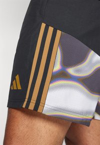 Schwarze Sportshorts mit braunen Streifen, die ein mehrfarbiges abstraktes Muster an der Seite aufweisen. Hergestellt aus leichtem Material mit einer glatten Textur.