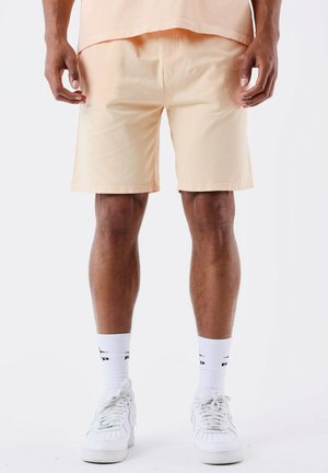 Pantalones cortos de algodón color durazno con un ajuste relajado, que cuentan con bolsillos laterales, una textura suave y dobladillo limpio. Combinados con zapatillas blancas y calcetas.