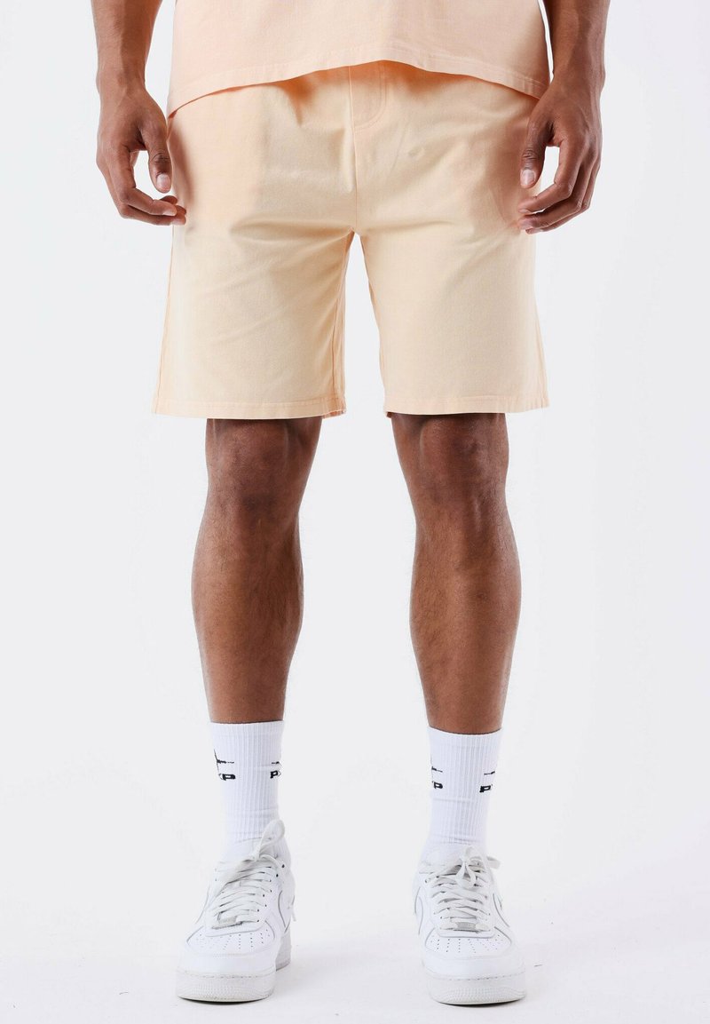 Pantaloni corti di cotone pesca con una vestibilità comoda, dotati di tasche laterali, una texture liscia e orli ben rifiniti. Abbinati a sneakers bianche e calzini.