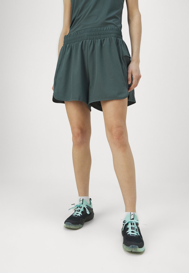 Roheline spordilühike, millel on elastne vöökoht, küljetaskud ja mugav lõige. Kombineeritud mustade sneakeritega, millel on mündirohelised aktsendid.