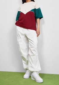 Röd och teal blockfärgad t-shirt med vita accenter, matchad med vita baggy-byxor och vita sneakers. Slät tygtextur.