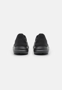 Chaussures de sport noires avec une tige en mesh texturé et des semelles en caoutchouc solides. Présente un talon rembourré et des accents de logo discrets. Vue de dos.
