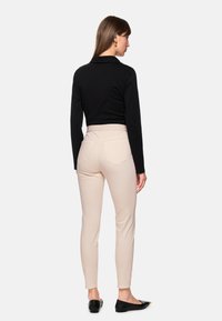 Black long-sleeve top, fitted at waist. Light beige pants with a smooth texture, featuring two back pockets. Black flats with a pointed toe.