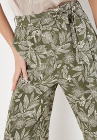 Grüne Blumenmuster-Hosen aus leichtem Stoff mit hoher Taille, seitlichen Taschen und einem gebundenen Gürtelakzent.
