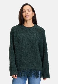 Dunkelgrüner Pullover aus strukturiertem, flauschigem Material. Verfügt über einen Rundhalsausschnitt und Fransenverzierungen am Saum. Lange Ärmel.