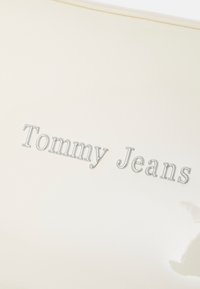 Busta bianca lucida con logo in rilievo argentato "Tommy Jeans". Caratterizzata da una texture liscia e una forma semplice e rettangolare.