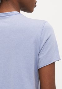 Tricou din bumbac de culoare albastru deschis, cu mâneci scurte, guler clasic rotund și o textură netedă. Design minimalist, fără modele vizibile sau accesorii.